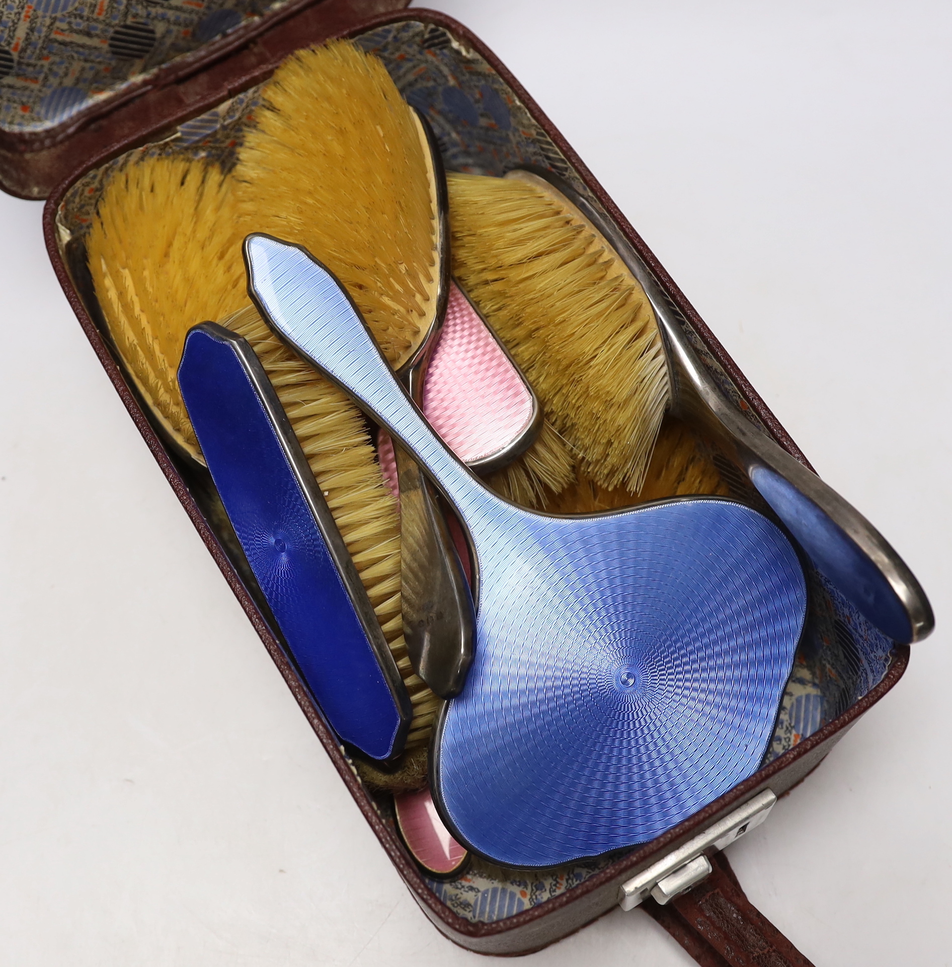 A George V silver and blue enamel five piece mirror and brush set, Birmingham, 1929 and a similar silver and pink enamel set, Birmingham, 1932.